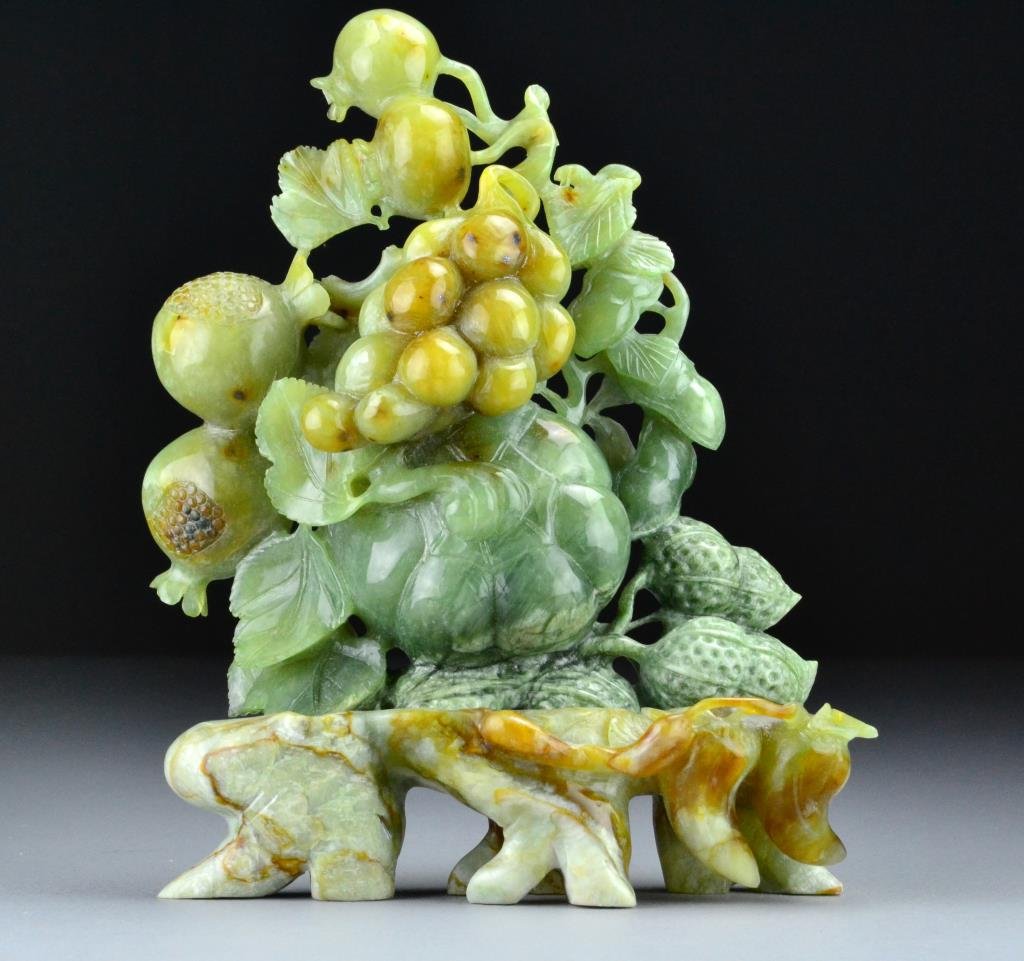 Chinese Jade Carving of Fruit: Finely carved celedon and russet jade depicting grapes, pomegranites and pumpkin resting on russet jade leaf form base, 9.5" H x 7.5" L, circa 20th century, good condition.