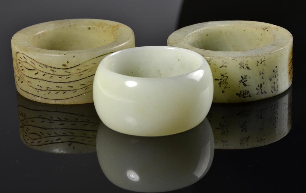 (3) Chinese Carved Jade Napkin Rings: Finely carved to depict characters and animal figures, one with no carving, largest is 2" outside diameter.