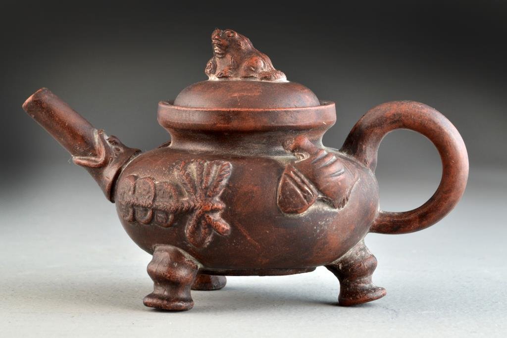 Chinese Yixing Pottery Tea Pot: Finely molded to depict bats and coins to the body, raised on shaped tripod feet, the finial molded as a foo-dog, the base and interior of the lid with impressed seal marks, 4.25"H X 7"W, circa late 1