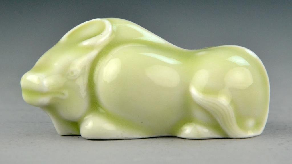 Chinese Celedon Glaze Porcelain Water Buffalo: Depicting a crouching bull with integrated horns, olive tinted celedon glaze, 1.75" H x 3.25" L, illegible impressed mark to bottom within an oval, circa early 20th century. Condition: good. Property 