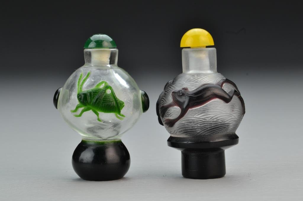 (2) Chinese Peking Glass Snuff Bottles: Having overlay of cricket and frogs, one with incised markings in background, each on .625" molded foot, complete with stoppers, tallest is 2.75"H. From the collection of David Bell who worked for an