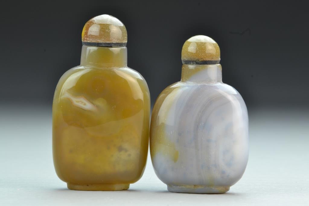 (2) Chinese Carved Agate Snuff Bottles: To include two finely carved and polished bottles, exhibiting natural swirling and lined properties of the stone, complete with matching stoppers, tallest is 2.875"H. From the collection of David Bell