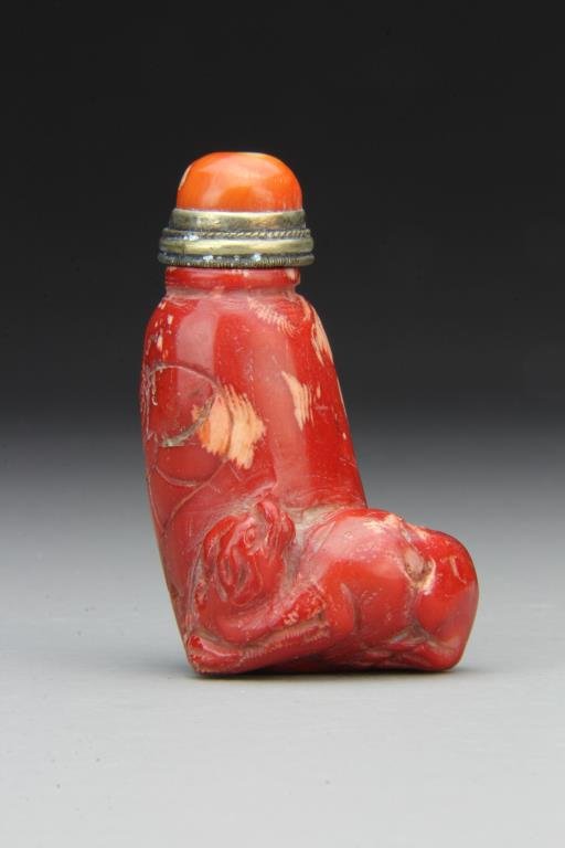 Chinese Carved Coral Snuff Bottle: Finely carved to depict reclining animal at base, incised flowers on reverse, complete with coral stopper and spoon with gilt ring, 3"H. From the collection of David Bell who worked for an Italian ste