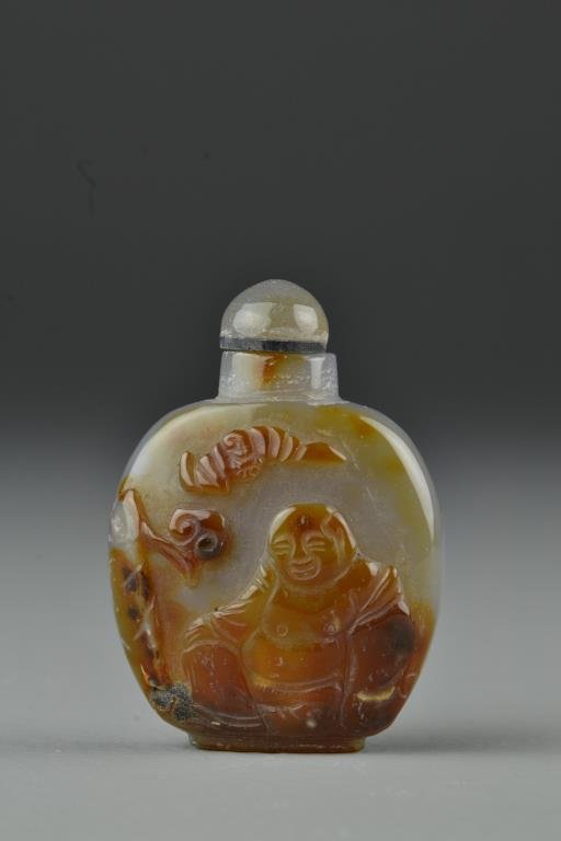 Chinese Carved Agate Snuff Bottle: Finely polished and carved to depict smiling Buddha with bat beneath tree, complete with matching stopper, 2.6"H. From the collection of David Bell who worked for an Italian steel company in China dur