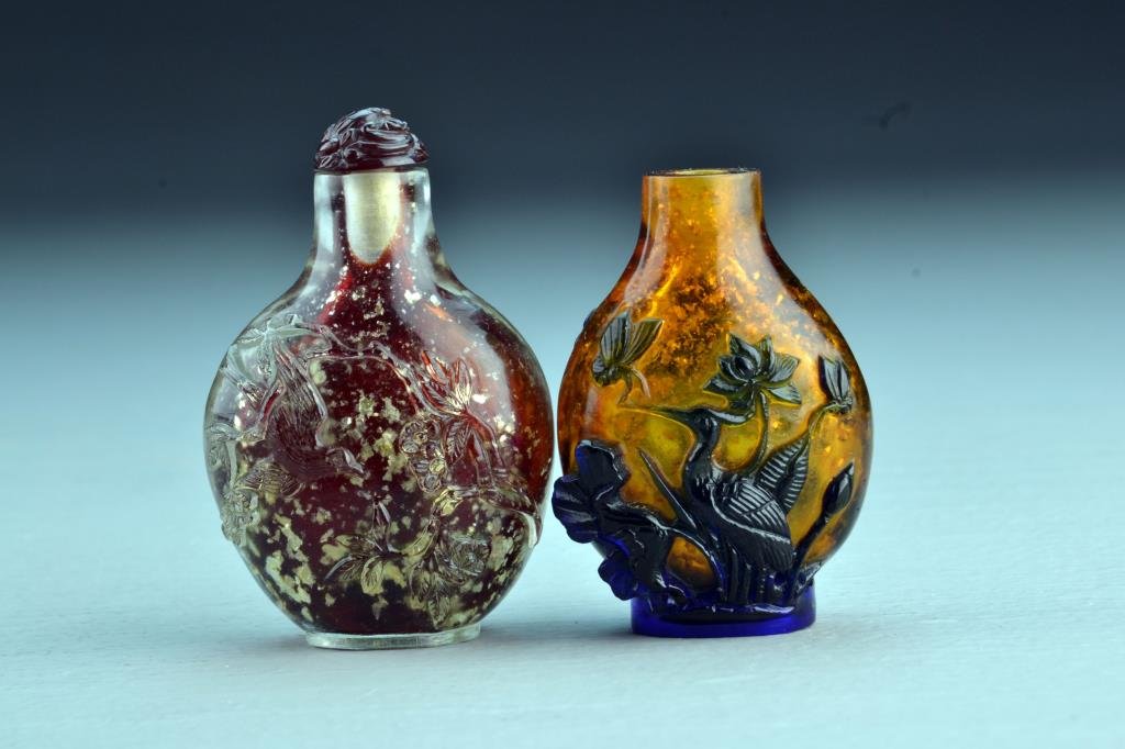 (2) Chinese Peking Glass Snuff Bottles: One with gold flecked appearance, carved to depict flowers and bird, other having overlay depicting crane, moth, and lotus flowers, tallest is 2.7"H. From the collection of David Bell who worked for a