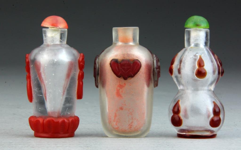 (3) Pcs Chinese Peking Glass Snuff Bottles: All finely carved with red decoration on clear glass depicting bats, the face of the beast, and non-objective decoration, largest measures 2.75"H. Condition, one lacking stopper.