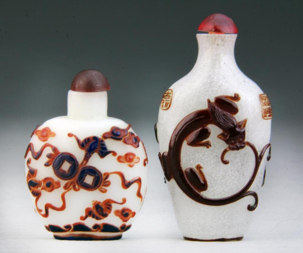 (2) Pcs Chinese Peking Glass Snuff Bottles: Each finely carved and having burnt umber colored decoration, one depicting foo lions in an ourosboros form, the other depicting bats contesting a coin amongst ruyi clouds and scholarly objects, large