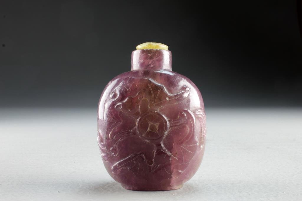 Chinese Carved Amethyst Snuff Bottle: Finely carved amethyst example with depictions of bats contesting a coin on both sides of bottle, complete with flat agate stopper, measures 2.75"H.