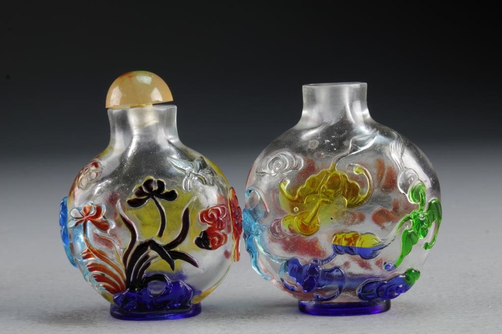 (2) Chinese Peking Glass Snuff Bottles: Two clear glass examples having polychrome overlay, one depicting bats with coins among ruyi clouds, the second example depicting lotus and other flowers among ruyi clouds, latter having beast head ha