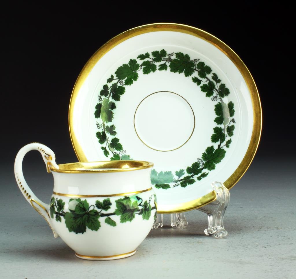 A Meissen Porcelain Cup & Saucer: Finely painted to depict a continuing band of leafy vines, having gilt trim swan formed handle, base bearing crossed swords in underglaze blue, saucer measures 1.25"H X 5.75"D, cup measures 2.25"H X 2