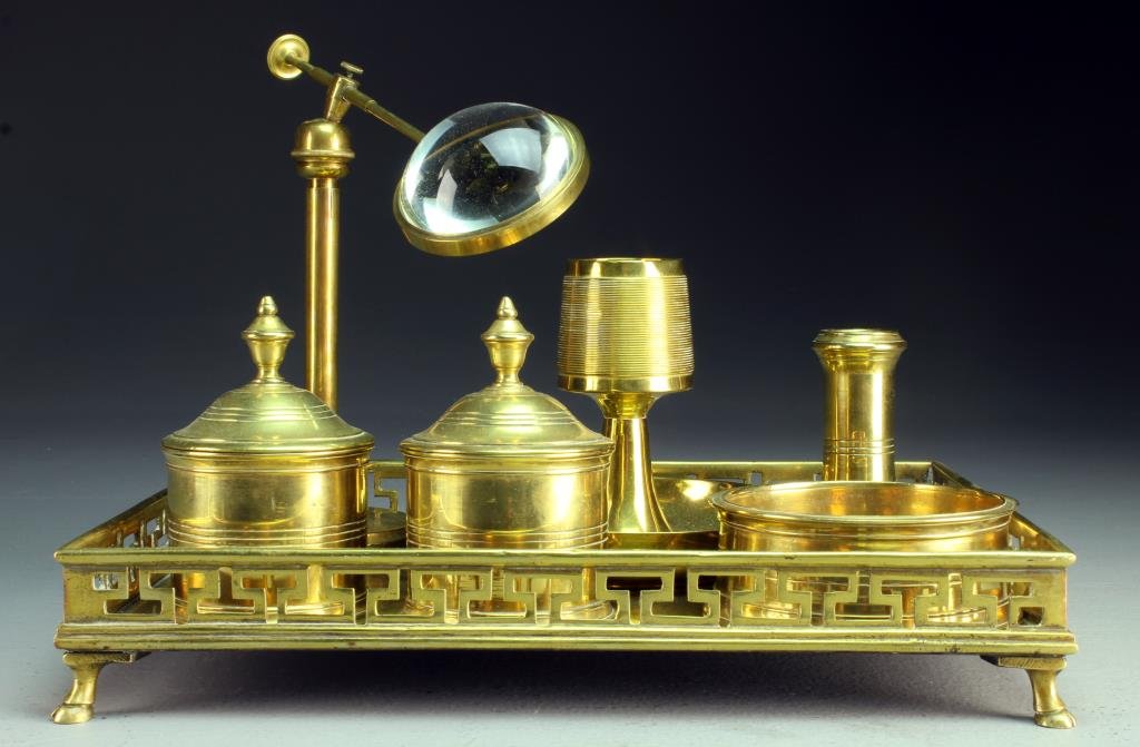 A 19th Century English Brass Desk Set: Having a brass gallerie tray raised on hoof feet and holding a match holderr and strike, a magnifying glass on stand, two covered containers, and a pen holder and more, tray measures 12.5"W x 9.5"D, c