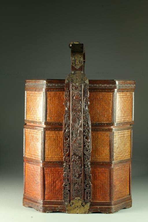 A Chinese Woven Wedding Basket: Having three tiers and a wood handle carved with a figural scene to sides, Greek key motif carved at base, having brass fixtures with pierced details, depictions of bats and a folding brass chilong ha