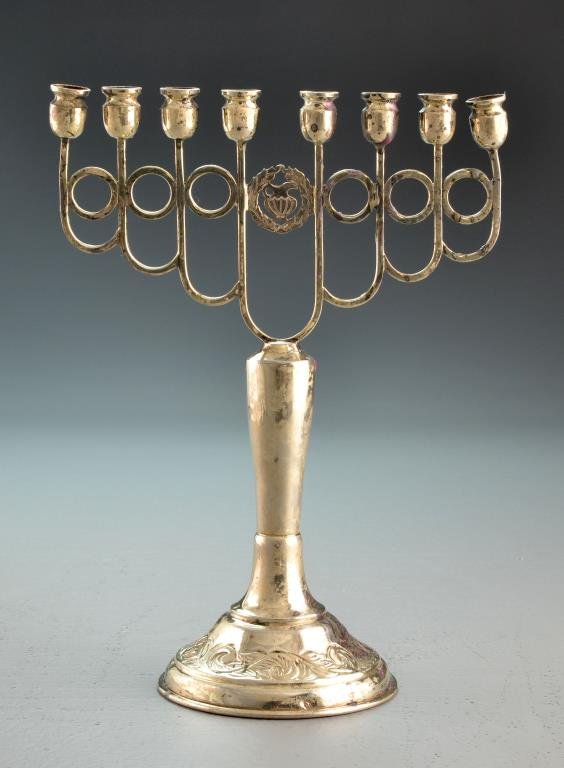 An Antique Sterling Silver Menorah: Having a pierced wreath and pitcher design flanked by eight candlesticks, raised on a baluster formed stem with circular base having stamped scroll decoration and Hebrew script, bears illegible mark t