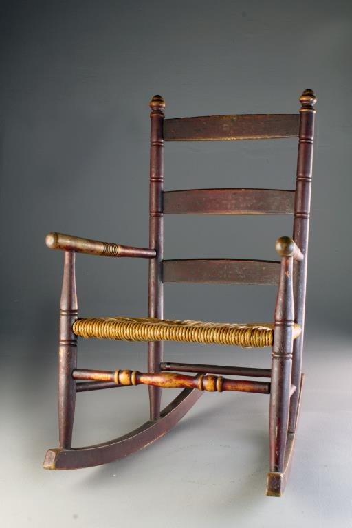 An American Antique Red Painted Child's Rocking Chair: Having turned stretcher and elements, having a rush seat and a three slat back, retaining most of it's original red paint, 24"H, circa 19th century.
