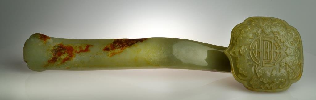 Chinese Qing Carved Jade Ruyi Sceptor: The shaped head carved to depict bats surrounding a shou symbol, the stone a celedon with russet patches, very well executed with finely carved details and a wonderfull polish. 14.625"L, circa 19th ce