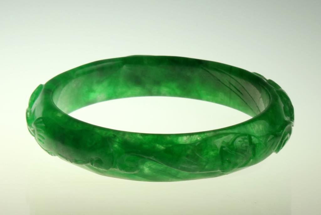 Chinese Jadeite Bangle Bracelet: Finely carved and polished from a deep apple green jadeite to depict bats and flowers, outside diameter 2.875", inside diameter 2.25".