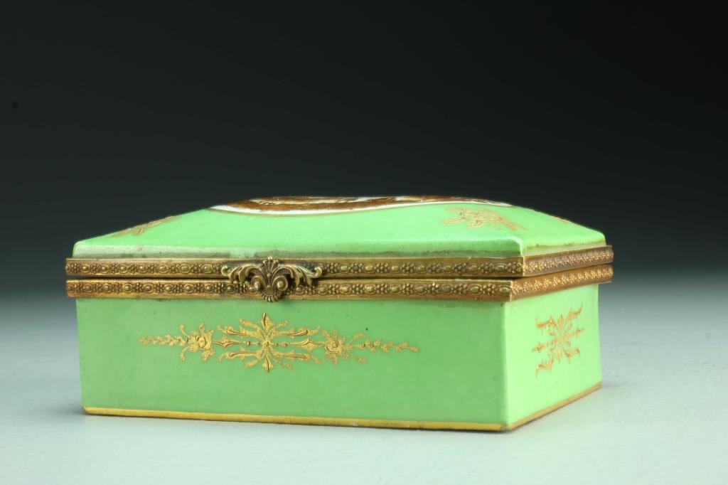 A Sèvres Painted Porcelain Dresser Box: A hinged porcelain box with raised gilt and enamel decoration, center panel depicting monochrome bucolic scene and signed "VP.", underside marked in blue with interlaced L's indicating the Sèvres fac