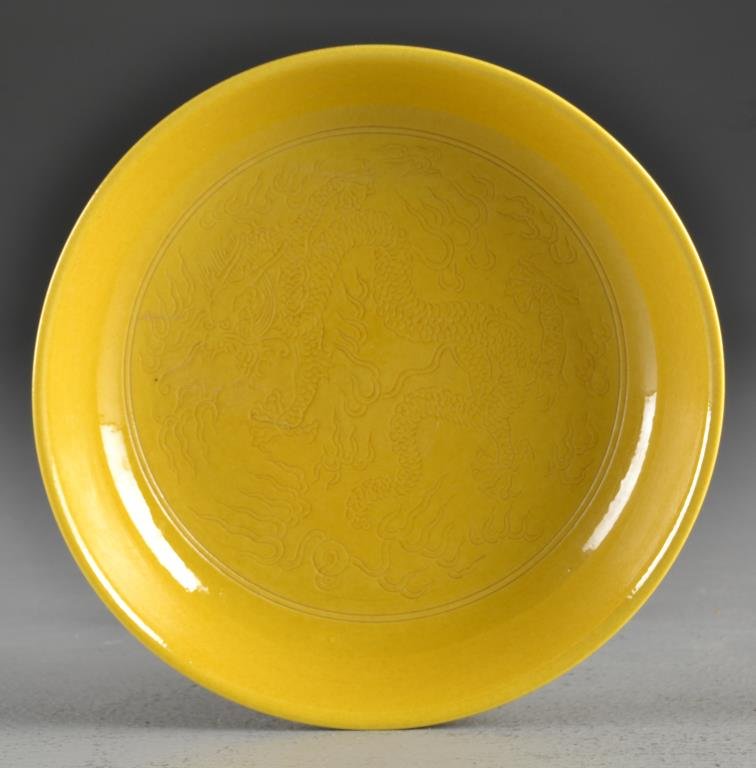 Chinese Qing Mustard Yellow Porcelain Saucer: Finely incised to depict a five clawed dragon chasing a flaming pearl, raised on short foot ring, base having Qianlong seal mark in underglaze blue, 1.5"H X 6.75"D, circa late 19th/early 20th century.