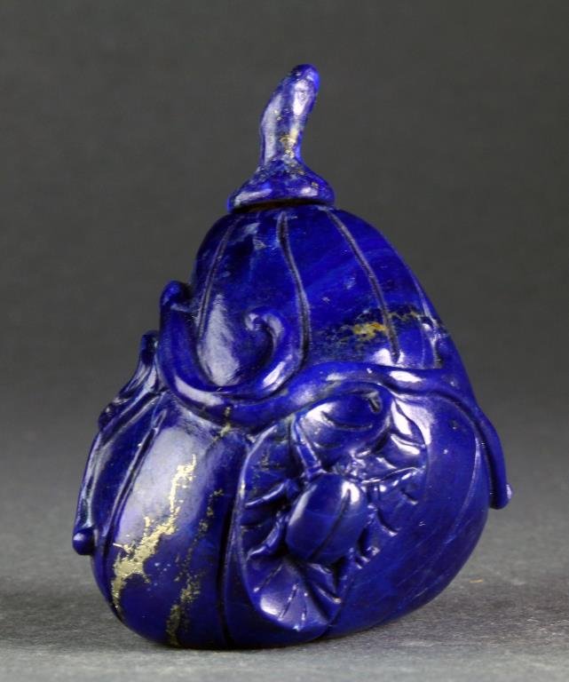 A Chinese Carved Lapis Snuff Bottle: Finely carved in the form of either a gourd or a fruit with incised lines, leaves vine and beetle carved in relief, complete with lapis stem formed stopper and having a bone spoon, measures 2.4"H.