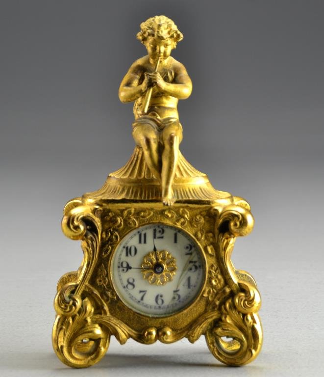A French or American Gilt Bronze Clock: Depicting a little boy playing the flute, having an enamel dial with Arabic Numerals and a scroll decorated case, measures 7.25"H , circa late 19th-early 20th century. Condition: with wear to gilt. Pr