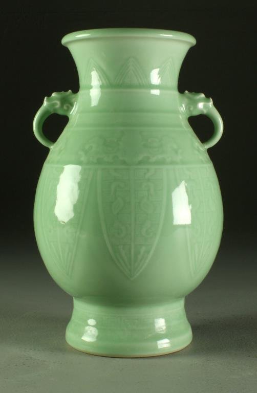 A Chinese Celadon Glaze Porcelain Vase: Molded after the original archaic bronze version, having molded decoration depicting dragons and stiff petals, having two dragon head handles and a seal mark in underglaze blue to underside, measures 