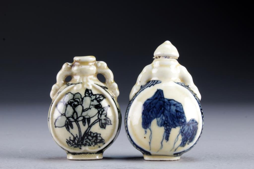 (2) Chinese Blue and White Porcelain Snuff Bottles: Formed as moonflasks, one painted at center to depict flowers with a base character marked in underglaze blue, the other depicting a cricket and bunches of grapes at center with a base marked by a blu