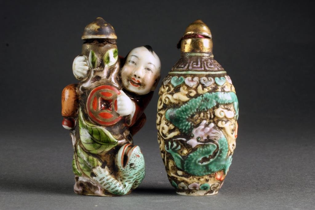 (2) Chinese Porcelain Snuff Bottles: One with molded surface painted to depict phoenix and dragon among ruyi clouds, the second example formed as smiling figure climbing bottle at center with frog at base and a coin in hand, bases four c