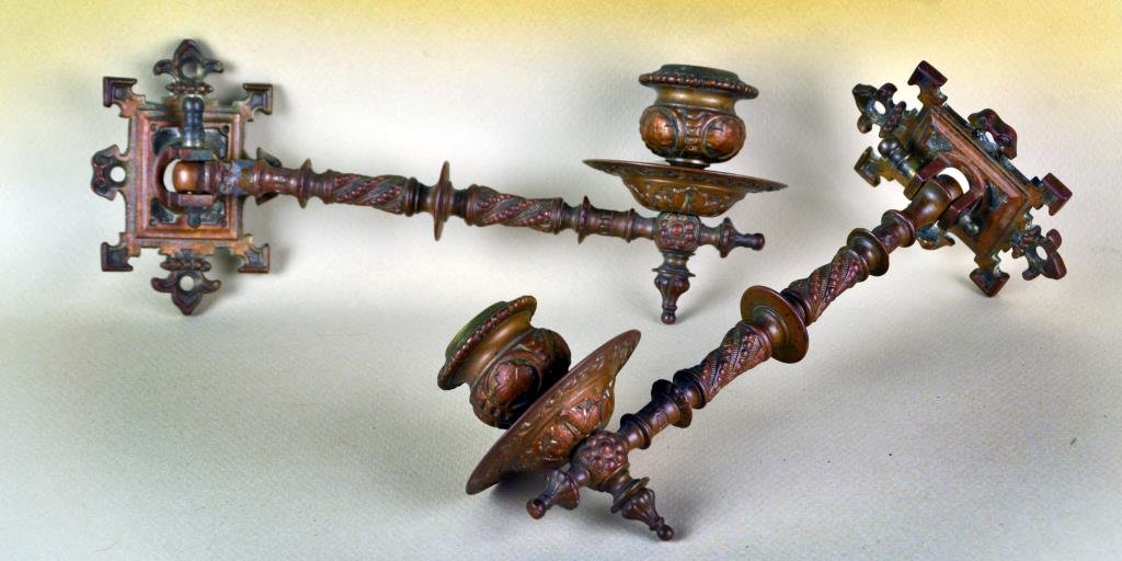 Pr Unique Brass Piano Sconces: A unique pair of ornate piano or wall candlestick sconces, having twisted beaded decoration along with floral and leaf motifs, wall mount having fleur-de-lis and pointed corners, having warm patina, a