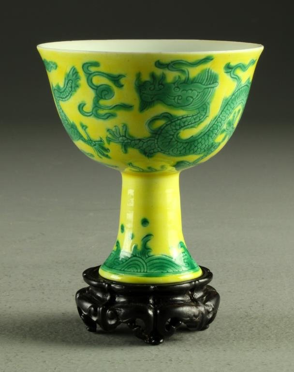A Chinese Chenghua Marked Porcelain Cup: Having finely incised dragons chasing a flaming pearl among ruyi clouds, against a yellow ground, having a Ming Chengua mark in underglaze blue to inside of foot, raised on carved hardwood stand, cup 