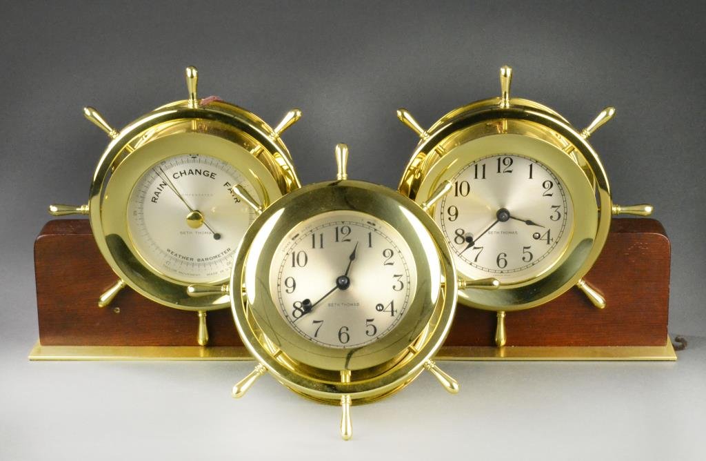 (3) Seth Thomas Brass Marine Clocks and Barometer: To include one brass Helmsman wall clock E537-001 resembling a Captain's wheel along with double-mounted brass clock E537-001 and barometer E537-009 mounted on walnut, largest is 9" H x 19" L, circa 2