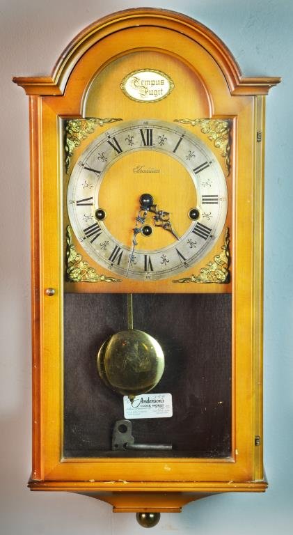 Franz Hermle Wall Clock: Having a glass door and glass panel to sides, a Roman numeral face with gilt metal decorations including "Tempus Fugit" plaque, movement marked Franz Hermle, bottom reverse of case marked West Germany