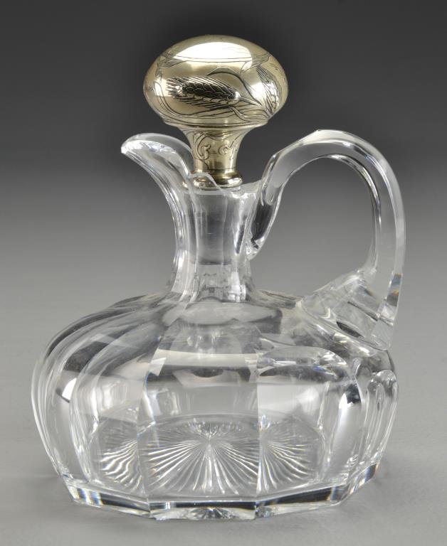 An Art Nouveau Crystal and Silver Mounted Jug: Having a faceted body and handle, holding an Art Nouveau sterling stopper decorated with cat tails and lily pads, measures 7.75"H, circa late 19th century. Property of a Birmingham, MI family.