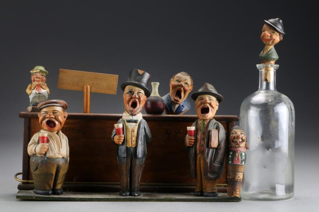 German Carved & Painted Wood Bar Set: Depicting a bar with comical caricature figures, bottle, bottle opener and stoppers, largest measures 9.5"H, circa early 20th century. Property of a Lapeer, MI couple.