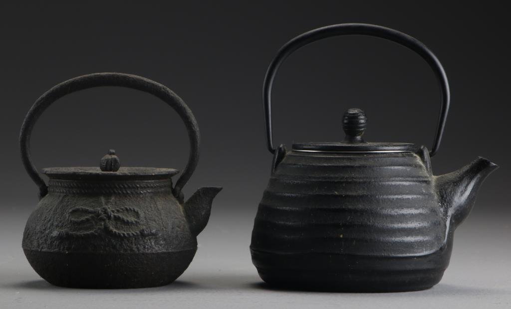 (2) Japanese Cast Iron Teapots: To include an antique example formed with a coiled rope tied in a ribbon to one side together with a more modern example having a ribbed body, tallest is 6"H. Property of a Lapeer, MI couple.