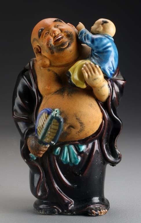 Chinese Republic Porcelain Figure: Depicting a Chinese deity holding a boy in one arm and a fan in the other, his robes having a deep aubergine glaze, the boys having a turquoise glaze, the belly and head left bisque, showing great att