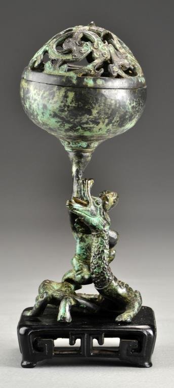 A Chinese Ming-Qing Bronze Figural Censer: Formed as a figure riding a dragon holding the censer above his head, formed in the archaic style but of the Ming or Qing dynasty, now raised on a later hardwood stand, 8.75"H not including the stand.
