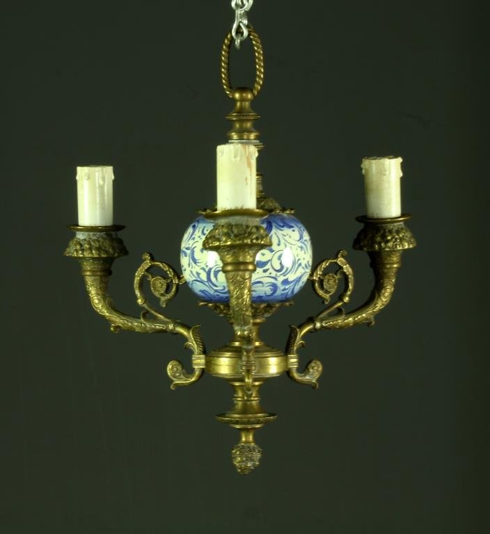 A Delft Porcelain & Brass Hanging Chandelier: A brass chandelier with three heavily scrolled arms and brass loop for hanging, having blue and white porcelain circular ball to center, now electrified, measures 12"H, circa early-mid 20th century. I