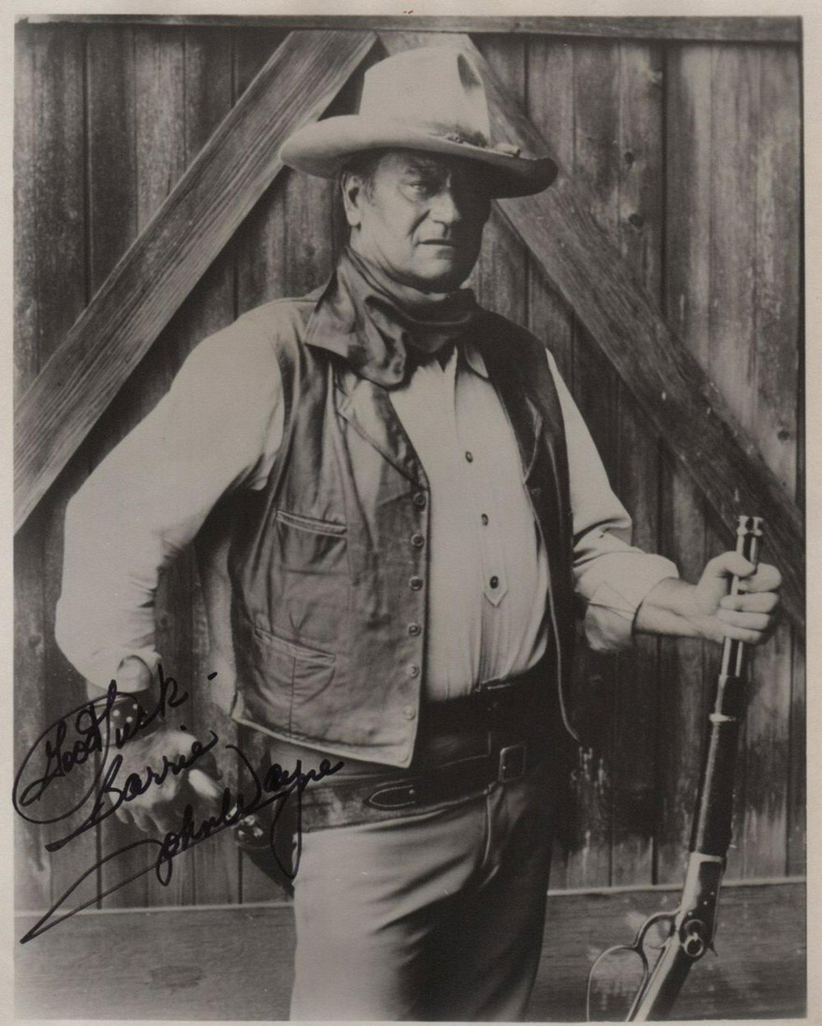 WAYNE JOHN: (1907-1979) American Actor, Academy Award: WAYNE JOHN: (1907-1979) American Actor, Academy Award winner. Signed and inscribed 8 x 10 photograph of Wayne standing in a three quarter length pose in cowboy costume and holding a rifle in one hand.