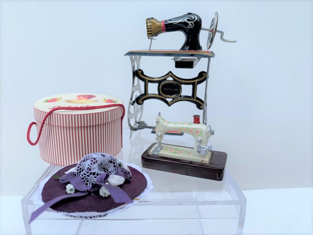 3 Sewing Machines w/ Hat & Hat Box, England: This lot of sewing machines include one from England which is the smaller painted sewing machine, a taller plastic and metal sewing machine, a tin sewing machine with dÃ©cor, a hand crafted hat and