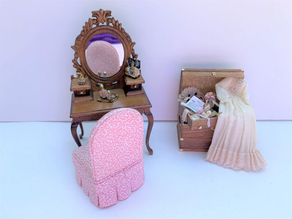 Ladies Vanity, Chair & Artisan Made Filled Trunk: This is a wooden vantity with a hand made slip cover chair in pink and white fabric. There's a jewelry box on the vanity as well as a perfume tray set. Next to that is a handmade wooden trunk with lad
