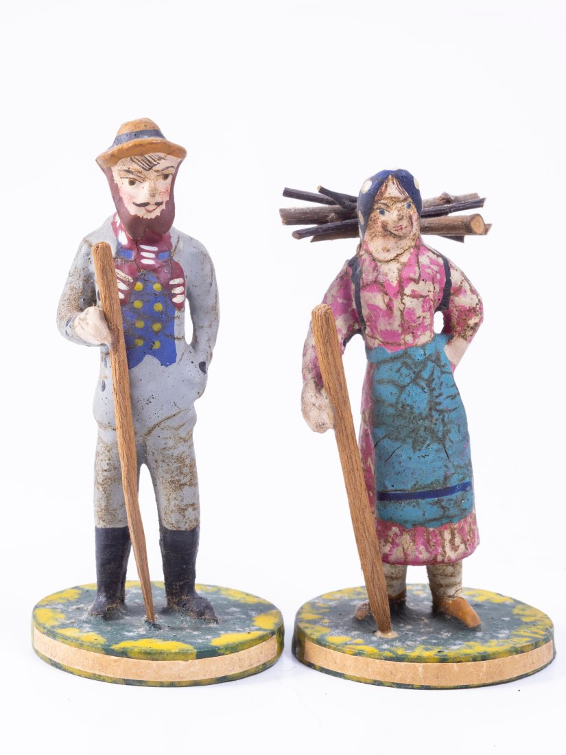 Wooden Painted Couple with Walking Sticks: Wooden painted couple in traditional clothing, holding walking sticks. Man has suit and hat, the woman has a handkerchief and is carrying sticks. Man 4 1/4" tall, Woman 3 7/8"