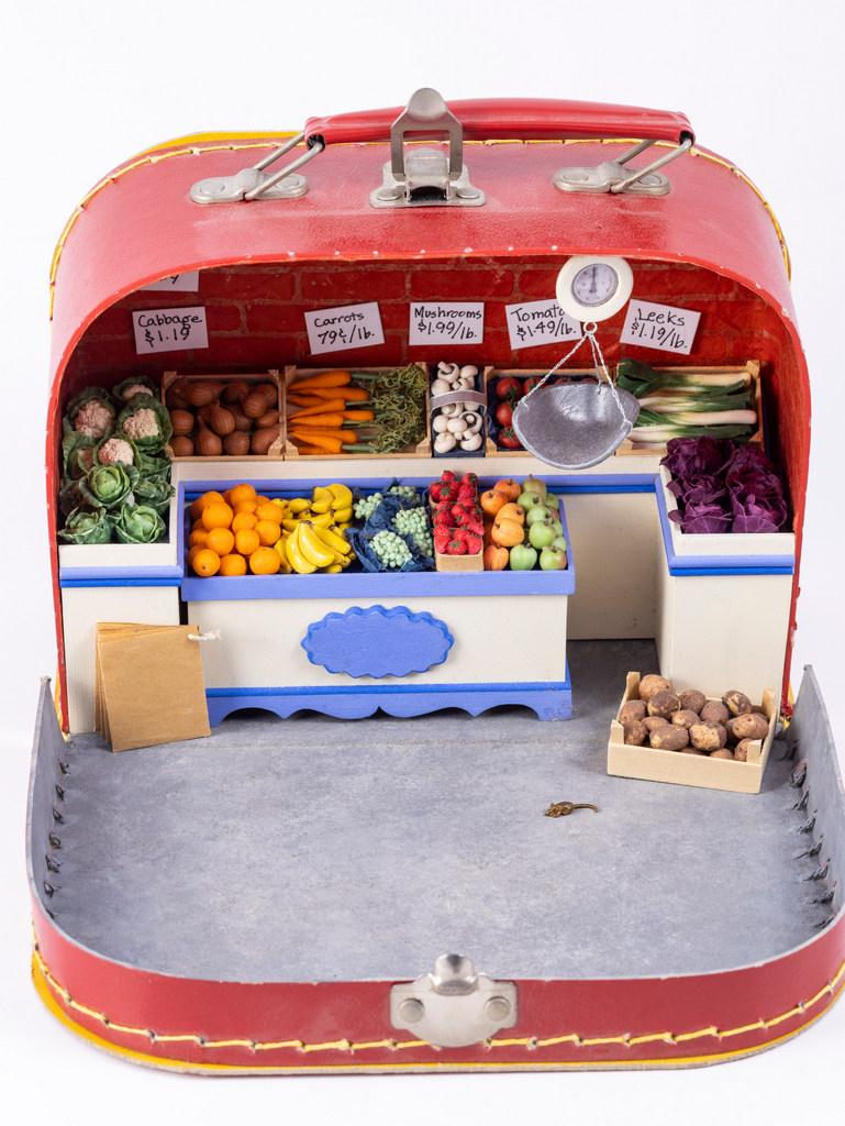 Terrific Box That Opens to a Grocer Shop: A variety of fruits and vegetables inside the lunch box. The vegetables are in a display and there's a hanging scale as well as a counter.