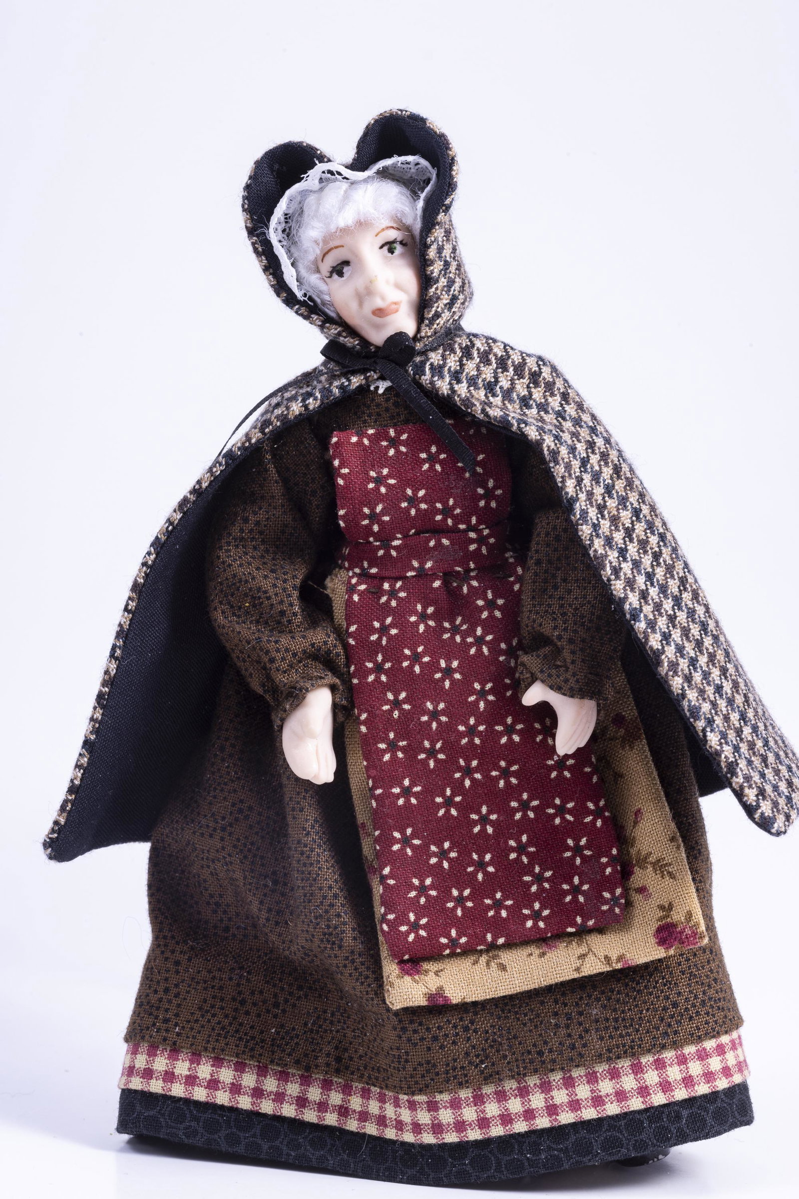 Older Woman Doll in Old Fashioned Outfit: This older woman dol has gray hair, wearing a brown dress with checkered patterned cape. She's made of porcelain.