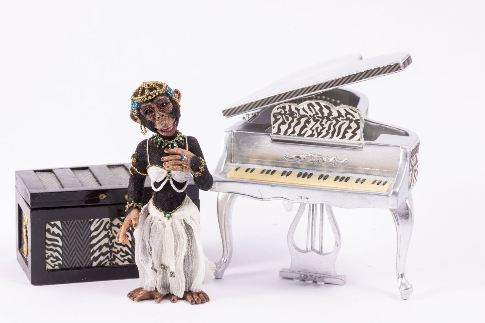 Todd Krueger Chimpanzee in Dress with Zebra Piano & Trunk: Todd Krueger female chimpanzee dressed in a white skirt and top with jewelry and beaded hat. There's a painted silver piano decorated with zebra paper and a matching zebra papered trunk.