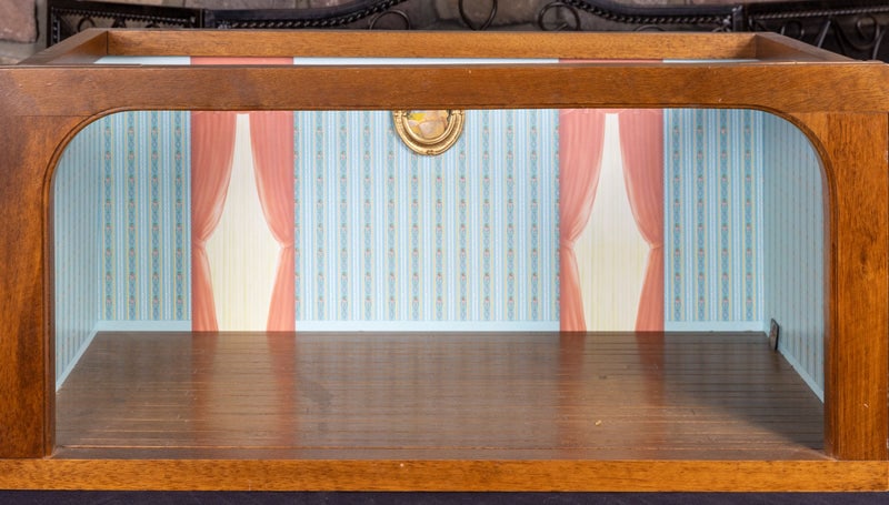 Roombox with Blue Striped Floral Wallpaper: This wooden roombox is pre-owned and decorated with blue striped floral wallpaper and two paper curtains. There's a picture in the middle of the windows that's attached. There's hardwood flooring. The