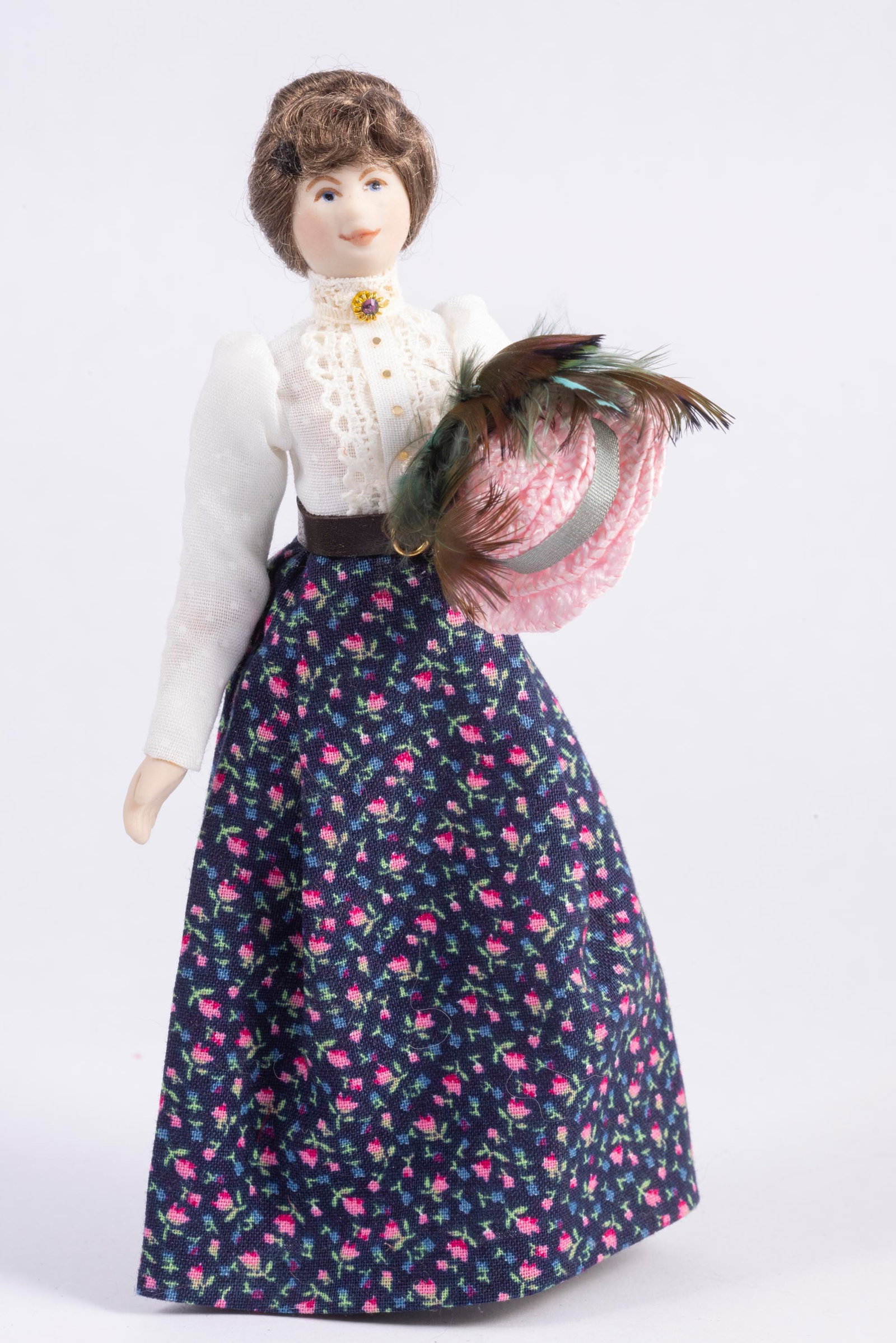Lady Doll Dressed In Floral Dress Holding Hat: Lady doll made of porcelain who's wearing a floral hat. She's holding a hat which can be removed and worn.