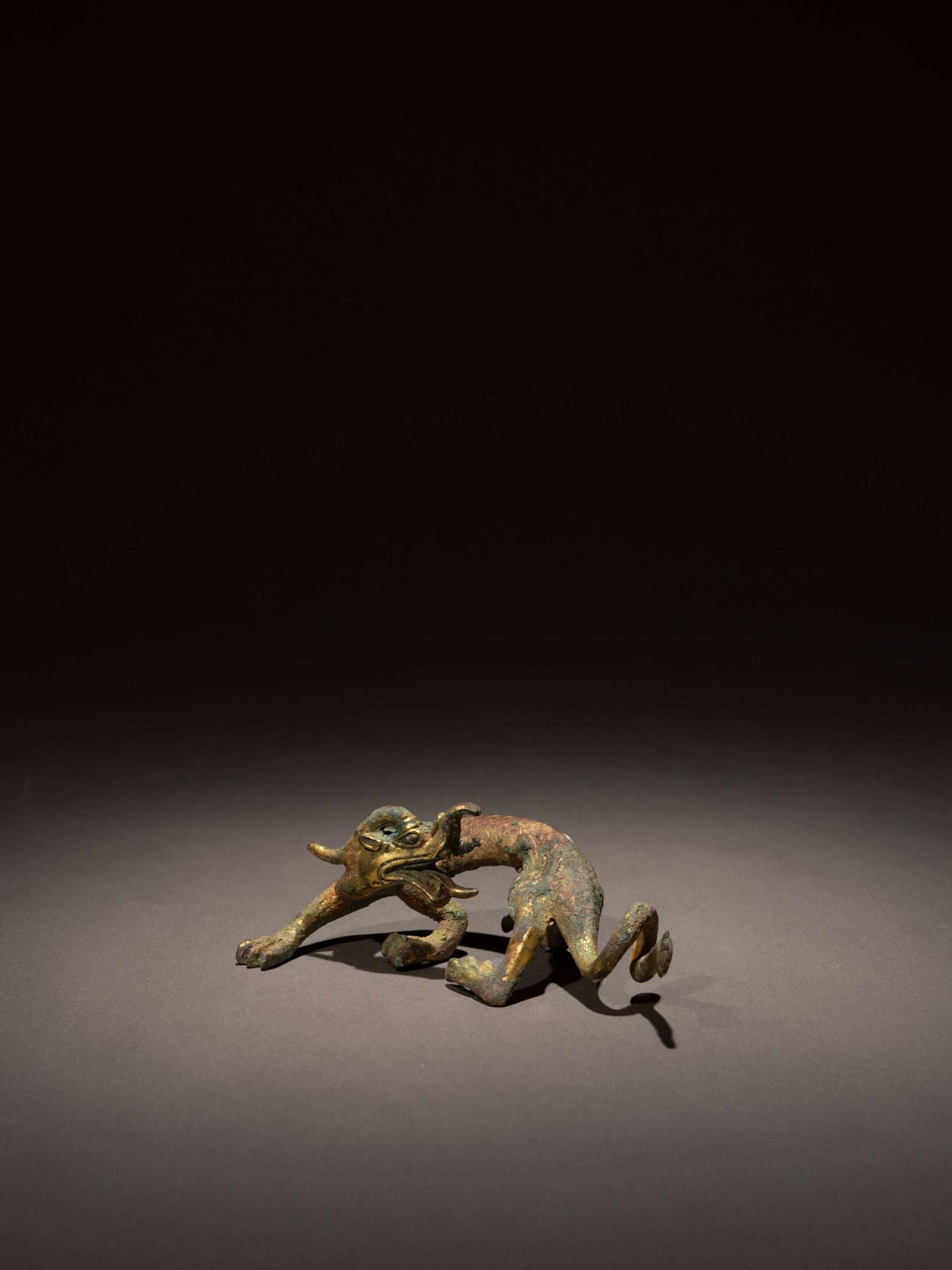 A GILT-BRONZE FIGURE OF A DRAGON: 年代(Age):TANG OR LATER 。尺寸(Size):13.4 cm Length, 4.7 cm Height。 參閱：唐 鎏金銅走龍，紐ಀ