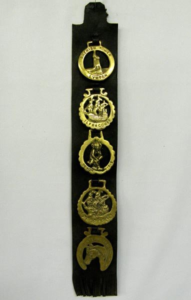 5 Vintage Horse Brasses On Leather Strap: 5 Vintage Horse Brasses On Leather Strap, largest brass measures approx. 3 1/2" x 3", leather measures approx. 23" long. From top to bottom brasses read: 1. "Rhenish Tower, Lynton" 2. "Ilfrancombe" 3.