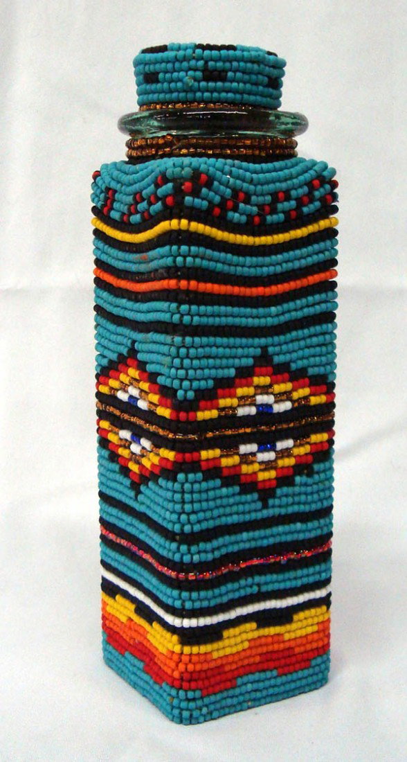 Beaded Glass Jar with Cork Lid by Kills Thunder: Beaded Glass Jar with Cork Lid by Kills Thunder. Beaded lid attached to bottle. Vibrant beadwork. 10.5'' x 3.75'' sq. Buyers Pay Actual Shipping and Handling Charges(see terms and conditions for more