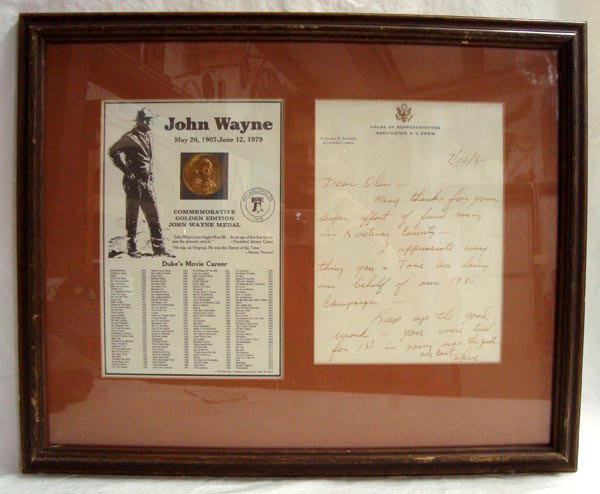 John Wayne Medal - Commemorative Golden Edition: John Wayne Medal - Commemorative Golden Edition. Framed gold medal with a listing of the Duke's movie career from 1928-1976. Additionally framed is a commendation letter from Steen D. Symms of Idaho a